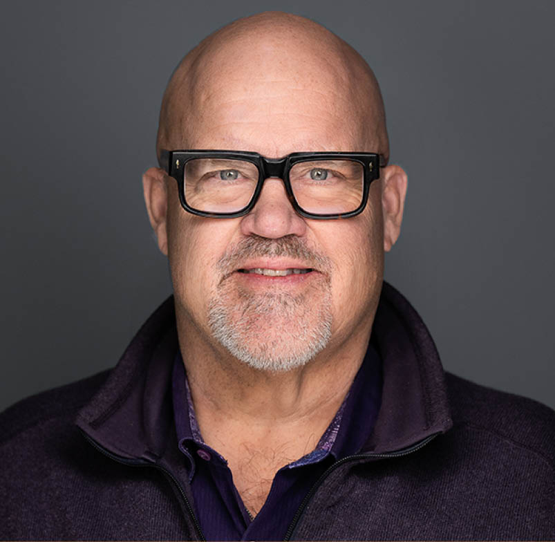 A man wearing glasses and a purple shirt. Description generated by AI