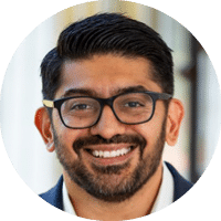 A man wearing glasses and a blue suit. Description generated by AI