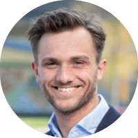 A man wearing a suit and tie standing in front of a building. Description generated by AI