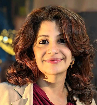 Person with long, wavy hair wearing a beige blazer over a maroon top in an indoor setting. Description generated by AI