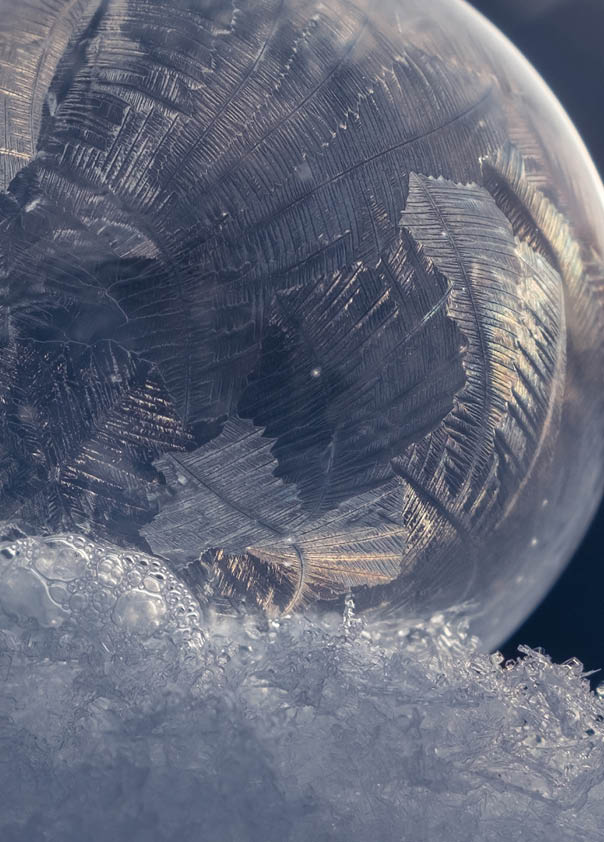 Frozen soap bubble with a beautiful pattern on the snow close-up on a blurry blue background. Selective focus