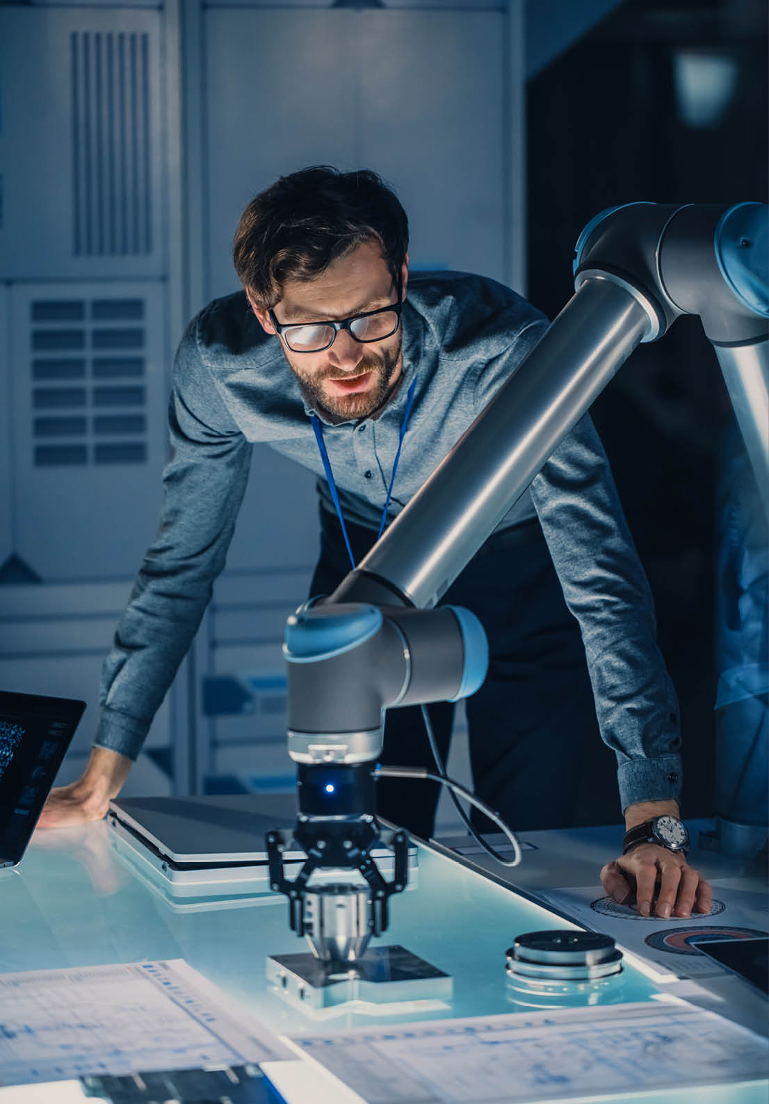 Vertical Shot of a Mechanical Engineer Works with Futuristic Robotic Arm and Programms it For Moving Metal Object. High Tech Research Laboratory with Modern Equipment.