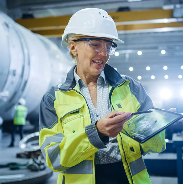 Professional Heavy Industry Female Engineer Wearing Safety Uniform, Holds Digital Tablet Computer and Explains Product Design. Industrial Factory Construction of Oil, Gas and Fuels Transport Pipeline