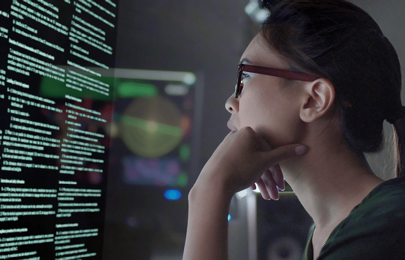 Stock photo of a young Asian woman looking at see through data whilst seated in a dark office