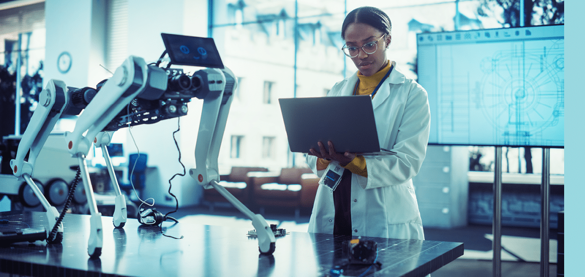 Portrait of Young Black Female Specialist in Lab Coat Using Laptop to Test an AI Robotic Prototype. Professional, Successful Woman Working as an Engineer in Modern High Technology Company Startup
